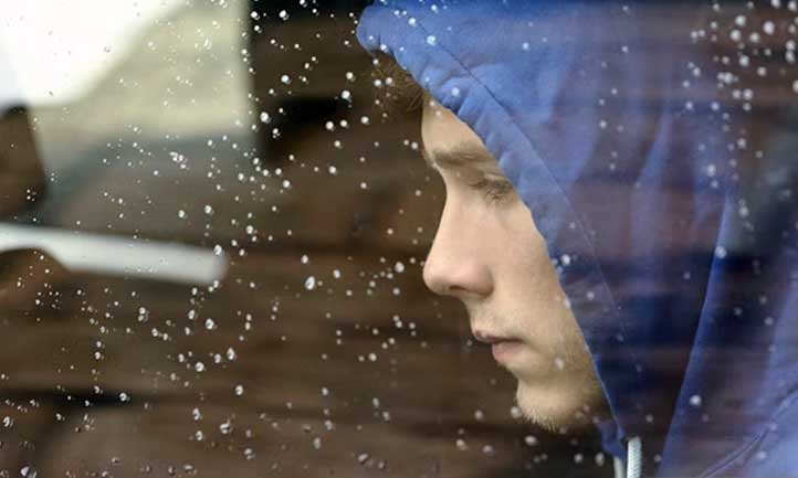 Teen looking out rainy window