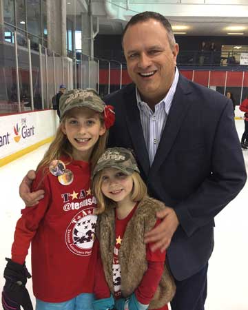 John is with TAPS survivors Christina Wilson, left, and Kate Wilson, at a skating party with the Washington Capitals in 2018. Christina and Kate lost their father, retired Navy Capt. David Wilson in 2014. 