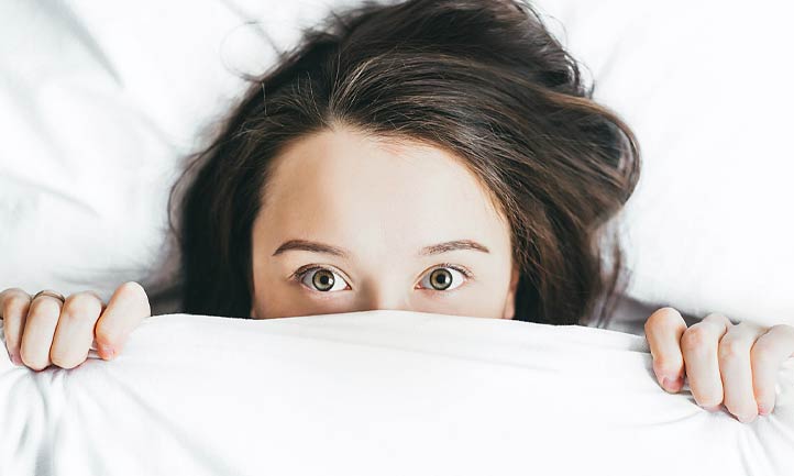 Women peeking out from under bed sheets