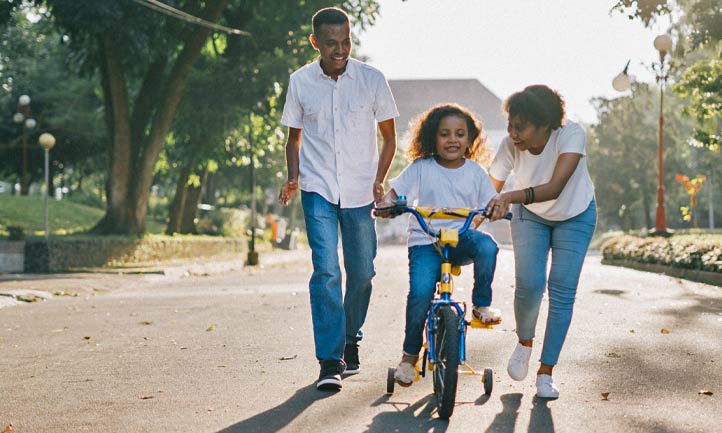 Family in park, little girl riding bike