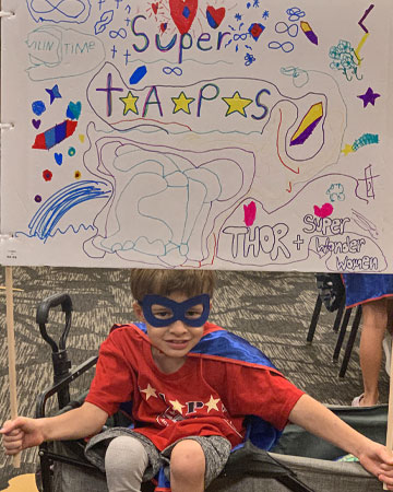 little boy in Superhero costume holds super TAPS sign