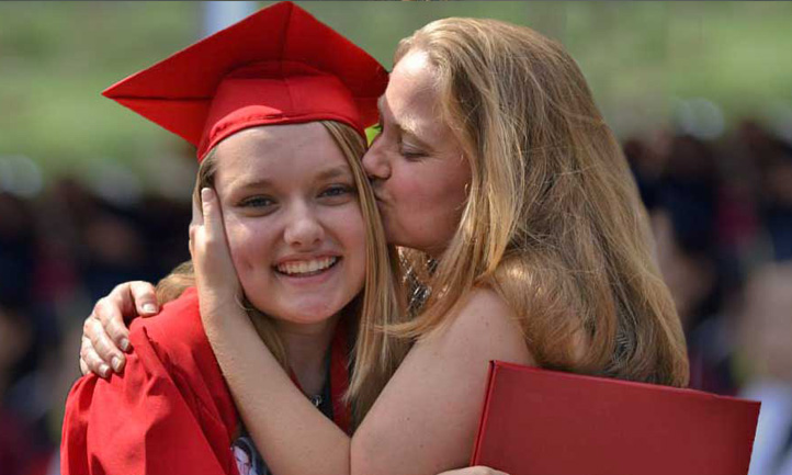 Student in grad gown hugged by mom